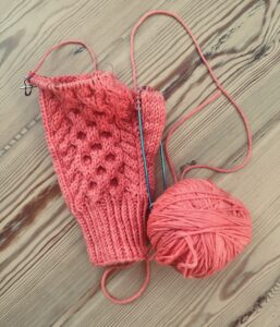 A partially completed hand knitted mitten with a ball of wool and circulat mittens