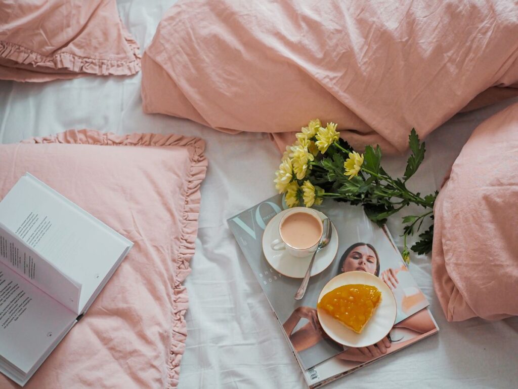 Picture of a bed with flowers, a magazine, a book and a cup of tea signifying selfcare