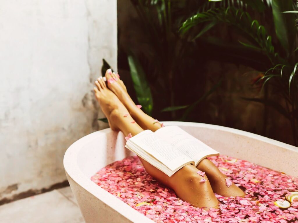 person lying in a bath filled with petals and reading a book